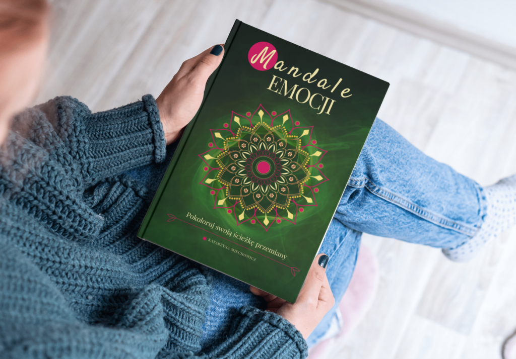 Kobieta siedzi na krześle, a na kolanach trzyma książkę Mandale Emocji - pokoloruj swoją ścieżkę przemiany